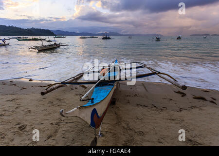 Outrigger Boote ankern in der Bucht bei Sonnenuntergang in Philippinen, Nahaufnahme eines am Strand hochgezogen Stockfoto