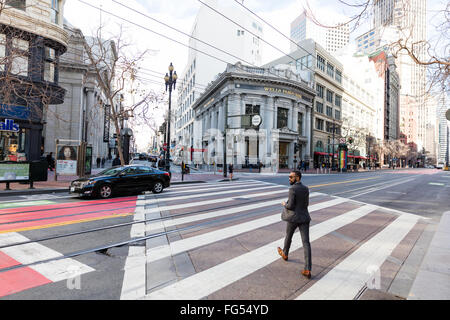 Junger Mann in einem Anzug überqueren einer Markt-Straße an der Front von der Wells Fargo Bank in San Francisco, Kalifornien Stockfoto