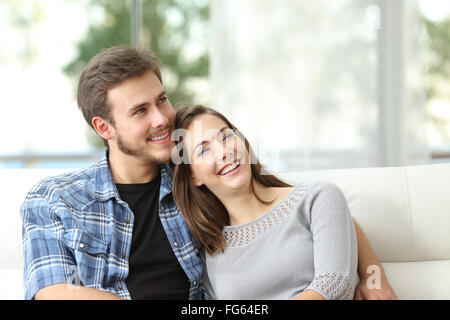 Glückliches Paar denken und aussehende seitwärts sitzen auf einer Couch zu Hause Stockfoto