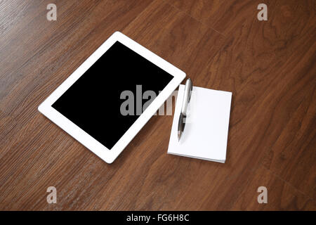 Digital-Tablette und Notizblock mit Bleistift auf einem Schreibtisch aus Holz. Stockfoto