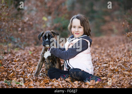 Boxer Welpen sitzen mit kleinen Mädchen im Herbst Blätter Stockfoto