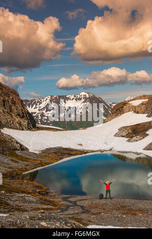 Ein Mann, der an Einem See mit ausgestreckten Armen in der Nähe des Harding Icefield Trail mit den Chugach Mountains im Hintergrund steht, Kenai Fjords Nati... Stockfoto