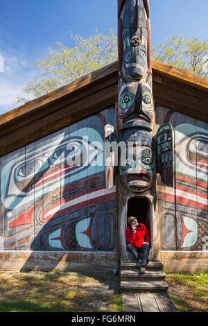 Mann sitzt auf den Stufen eines Tlingit-Clan-Hauses mit Smartphone-Totem Bight Historic State Park, Ketchikan, südöstlichen Alaska, USA, Frühling Stockfoto