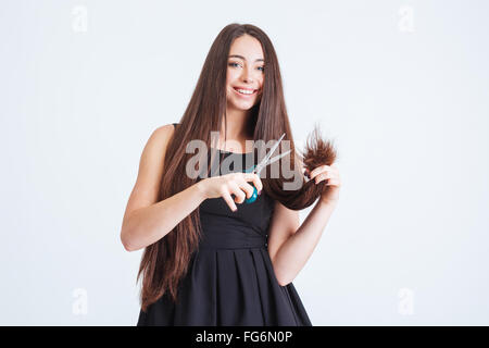 Fröhliche hübsche junge Frau schneiden Spaltung Enden der langen, dunklen Haare mit einer Schere auf weißem Hintergrund Stockfoto