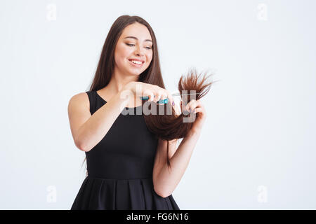 Lächelnde schöne junge Frau mit langen, dunklen Haare schneiden Teilung endet mit einer Schere auf weißem Hintergrund Stockfoto