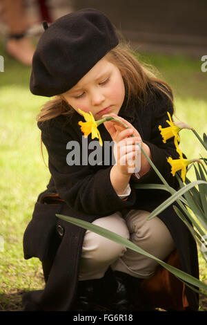 Portrait of Young Girl Dressed in A Brown Overcoat, Hose and Beret ist Holding A Yellow Daffodil mit einer Hand und streichelte es mit der anderen, C... Stockfoto