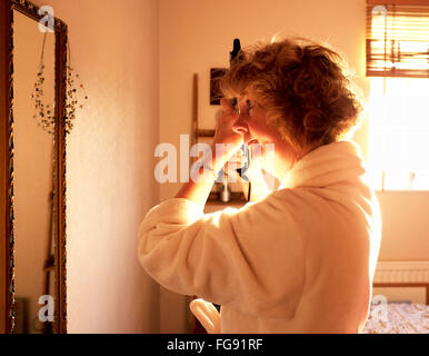 Applying Reife Frau macht ihr Haar morgens mit einer beheizten Curling Zange im Schlafzimmer Stockfoto
