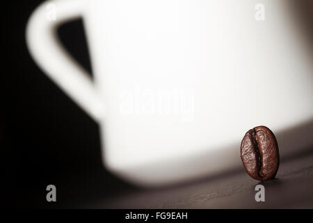 Makroaufnahme einer Kaffeebohne mit Milchkaffee Tasse Silhouette im Hintergrund Stockfoto
