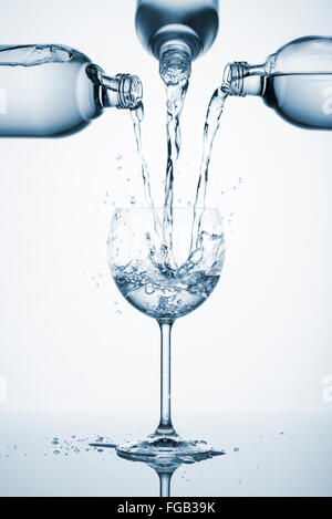 drei Flaschen gießen Wasser in Glas mit Spritzern, mit blauem Licht Stockfoto