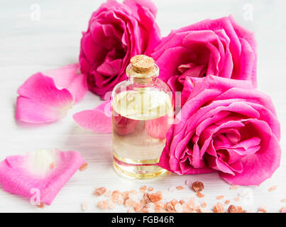 Rosenwasser in einer Glasflasche mit Rosen und zarten Blütenblätter Stockfoto