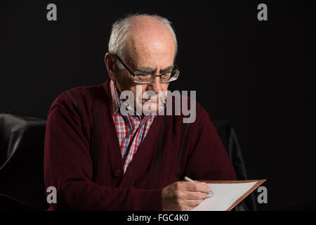 Alter Mann tragen Brillen schreiben einige Mitteilungen mit Pfanne und White paper Stockfoto