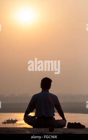 Meditieren, Meditation/Meditating / Yoga bei Sonnenaufgang mit Blick auf Fluss Ganges. Die Kultur von Varanasi ist eng verbunden mit dem Fluss Stockfoto