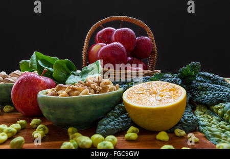 Rote Äpfel in einem Korb, Walnüsse, halb orange und Wasabi Erbsen auf Holztisch mit schwarzem Hintergrund Stockfoto