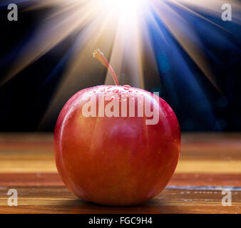 Rot-Fuji-Apfel mit Wassertropfen und leichte Flare auf Holztisch mit schwarzem Hintergrund Stockfoto