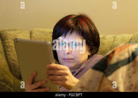 Hausfrau mittleren Alters Frau ungeschminkt lesen Nachrichten auf Tablette abends zu Hause auf sofa Stockfoto