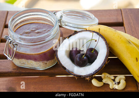 Kirsche Kokos Banane über Nacht Hafer mit gerissenen öffnen Coco, Banane, Cashew-Kerne gemischt mit Chia Samen und Kirsche Sahne in einer Mason j Stockfoto