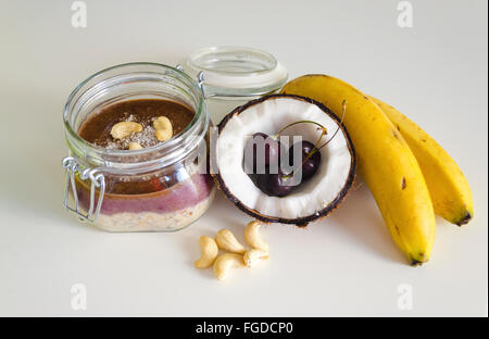 Kirsche Kokos Banane über Nacht Hafer mit gerissenen öffnen Coco, Banane, Cashew-Kerne gemischt mit Chia Samen und Kirsche Sahne in einer Mason j Stockfoto