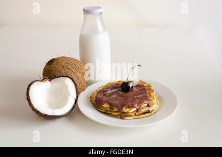 Frühstück und Brunch Kokos Pfannkuchen essen mit gerissenen Coco, Glasflasche Milch und Kirsche auf weißem Hintergrund zu öffnen. Stapel von Stockfoto