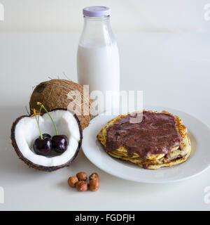 Frühstück und Brunch Kokos Pfannkuchen essen mit gerissenen Coco, Glasflasche Milch und Kirsche auf weißem Hintergrund zu öffnen. Stapel von Stockfoto