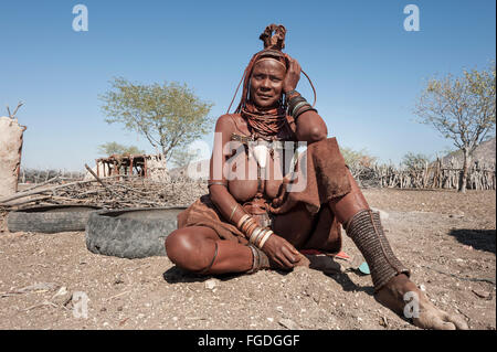 Porträt einer Himba Frau sitzen auf dem Boden ihres Dorfes. Stockfoto