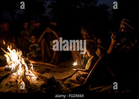 Gruppe von Personen aus dem San-Stamm, auch bekannt als "Buschmänner", sitzen um das Feuer in der Nacht zu rauchen und erzählen Geschichten. Stockfoto