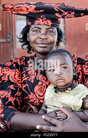 Porträt einer Herero-Frau mit Trachtenmode hält ihr Kind. Stockfoto