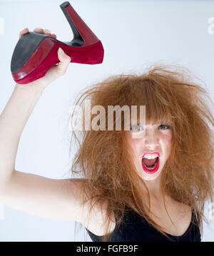 Frau mit strubbeligem Haar hält einen roten Wildleder high hochhackigen Schuh in die Luft schlagen, schreien Stockfoto