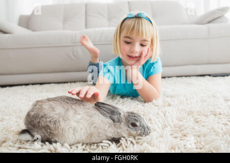 Kleines Mädchen liegend auf Teppich die Kaninchen streicheln Stockfoto