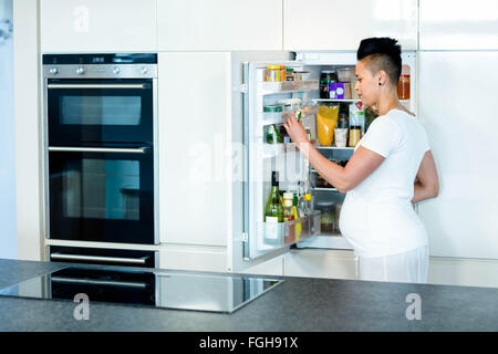 Schwangere Frau auf der Suche nach Essen im Kühlschrank Stockfoto