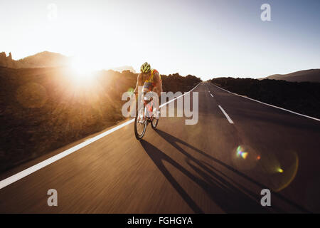 Ein Radfahrer fährt Rad auf einer leeren Straße direkt vor Sonnenuntergang Stockfoto