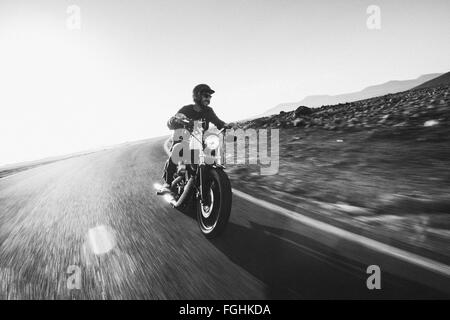 Mann reitet auf seinem Motorrad auf einer leeren Straße in der Wüste Stockfoto