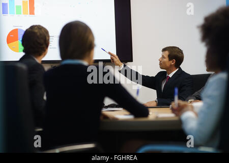 Gruppe von Geschäftsleuten treffen in corporate Konferenzraum, lächelnd während einer Präsentation. Die Mitarbeiter sind Diagramme untersuchen. Stockfoto