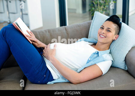 Porträt der schwangeren Frau ein Buch auf dem Sofa liegend zu lesen Stockfoto