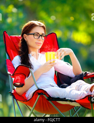 Schöne Frau ruht im Freien, auf dem Stuhl sitzen und Tee trinken, Sommer Urlaub im camp Stockfoto