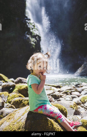 Junges Mädchen etwa 1,5 Jahre alt posieren für ein Porträt unter einem hohen Wasserfall im Umpqua National Forest in Oregon. Stockfoto