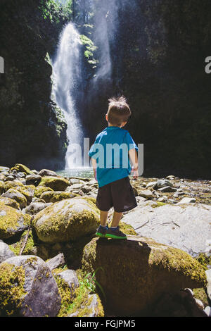Drei Jahre alter Junge stehend auf der Basis eines großen Wasserfalls im Umpqua National Forest in Oregon. Stockfoto