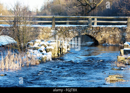 Detail der Blidingsholm Stein Bogen, dass Kreuze Brücke den Fluss Morrumsan. Dünne Schicht Schnee bedeckt den Boden und Steinen. Kleine Stockfoto