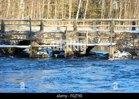 Detail der Blidingsholm Stein Bogen, dass Kreuze Brücke den Fluss Morrumsan. Dünne Schicht Schnee bedeckt den Boden und Steinen. Woode Stockfoto