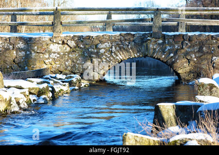 Detail der Blidingsholm Stein Bogen, dass Kreuze Brücke den Fluss Morrumsan. Dünne Schicht Schnee bedeckt den Boden und Steinen. Kleine Stockfoto