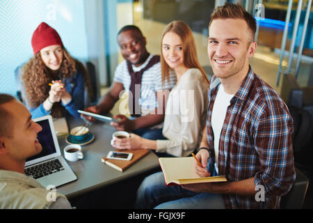 Glücklicher Kerl mit Blick in die Kamera, während seine Freunde in der Nähe von entspannenden notepad Stockfoto