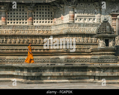 Eine junge Frau in einem orange sari Spaziergänge entlang der kunstvoll gravierte Tempel Wände an einem sonnigen Tag in Indien Stockfoto