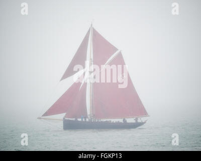 eine klassische Yacht segelt in volle rote Segel durch Nebel Nebel auf einer grauen grauen Armen Visibity Wetter im Solent, UK Stockfoto