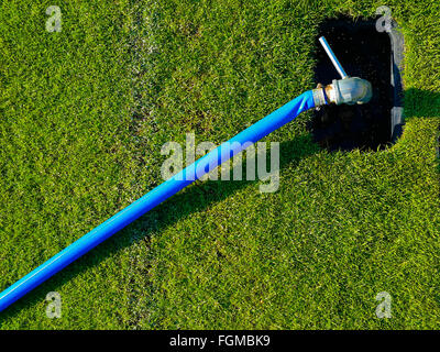 Blaue Kunststoff-Schlauch mit Ventil in Runde Rechteck-Loch auf dem grünen Rasen-Fußballplatz am Nachmittag Sonneneinstrahlung verbunden Stockfoto