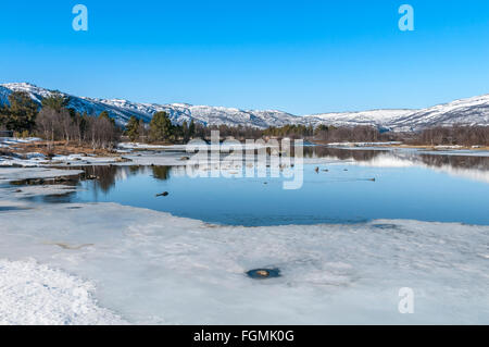 Blick von der Brücke zur Stadt Geilo, bei Ustedalsfjord, südlich von Zentrum der Stadt, Eis schmelzen am Fluss, Skipisten auf Hügeln, Norwegen. Stockfoto