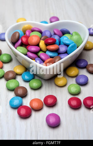 Bunten Schokoladen Smarties in einer herzförmigen weißen Schale, Schüssel. Stockfoto