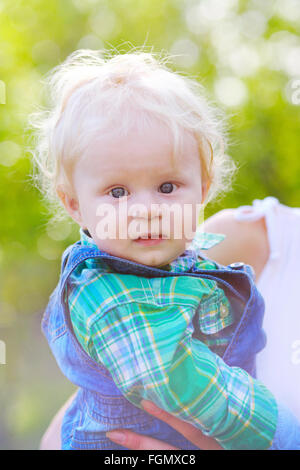 Mutter hält das Kind an Händen im Freien. Das Kind schaut in die Kamera Stockfoto