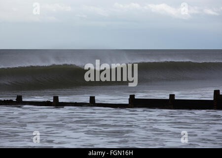 Eine Welle bricht durch eine hölzerne Buhne am Strand von Blyth in Northumberland, England. Stockfoto