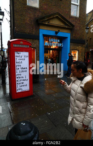 Asiatische tourist Smartphone Neben alten roten Telefonzelle mit wrdsmth Angebot Holding, Seven Dials, in der Nähe von Covent Garden, London, England Stockfoto