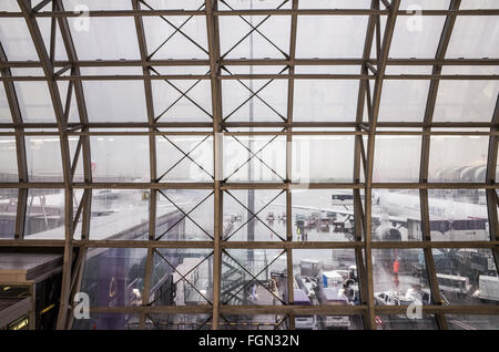 Fensterblick auf den Suvarnabhumi-Flughafen in Bangkok, Thailand | BANGKOK, Thailand — Ein Blick aus einem Fenster im Suvarnabhumi-Flughafenterminal bietet einen Ausblick auf das Flughafengelände. Flugzeuge, darunter eines von China Airlines, und Bodendienstgeräte sind auf dem nassen Boden zu sehen, zusammen mit Flugpersonal. Der Suvarnabhumi-Flughafen (BKK) ist einer von zwei internationalen Flughäfen, die Bangkok bedienen, und ist Thailands wichtigstes internationales Tor. Er liegt in der Provinz Samut Prakan und ist ein wichtiger Luftverkehrsknotenpunkt für Südostasien, bekannt für seine unverwechselbare Architektur. Stockfoto