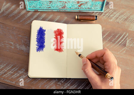Retro-Effekt und getönten Bild einer Frau hand Zeichnung Frankreich Flagge am Notebook mit einem Füllfederhalter auf einem Notebook. Konzept-Bild mit Handzeichnung der Frankreich-Flagge Stockfoto